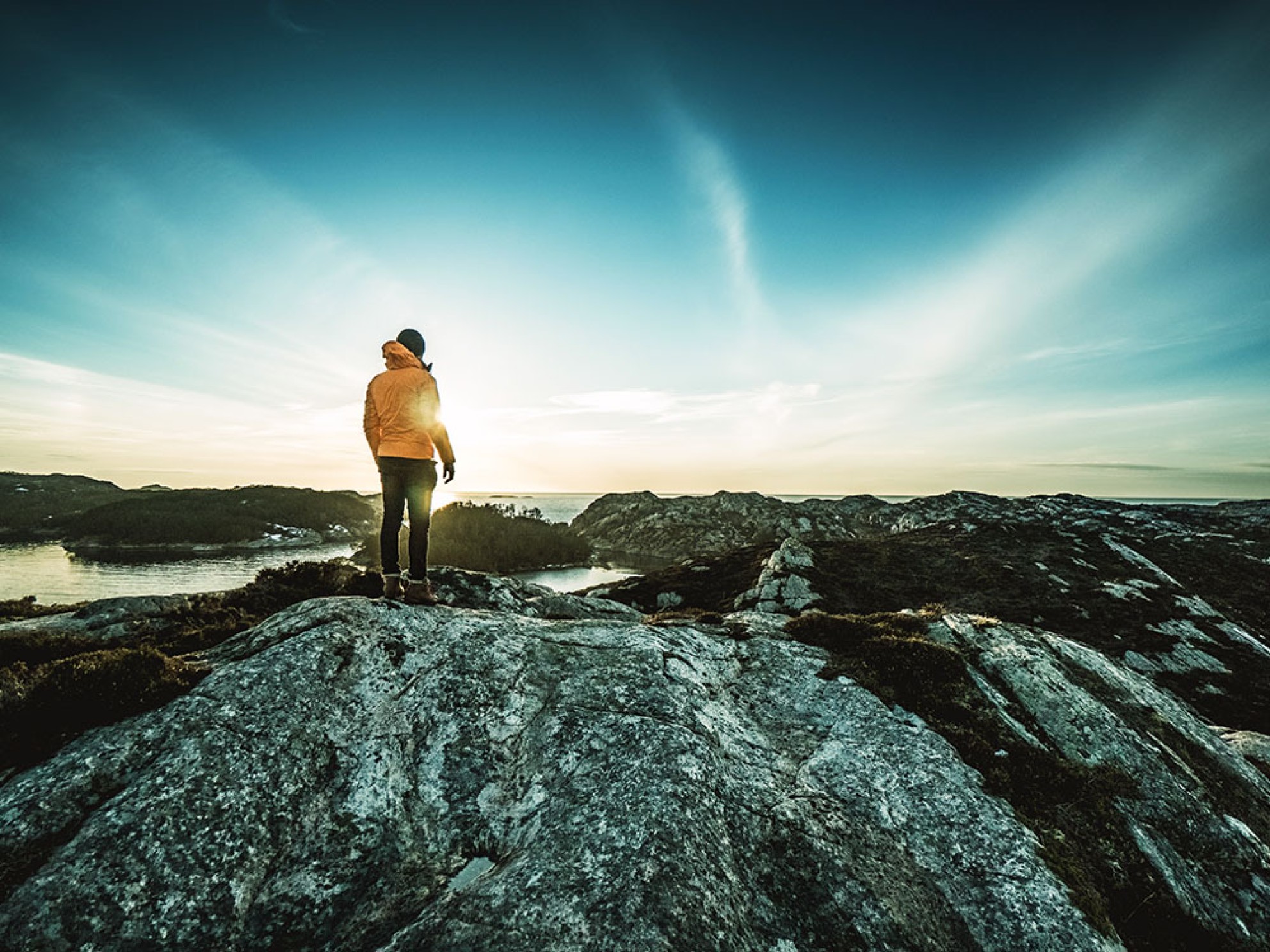 A person in hiking clothes, trekking through a mountain landscape, looks out over a fjord.
